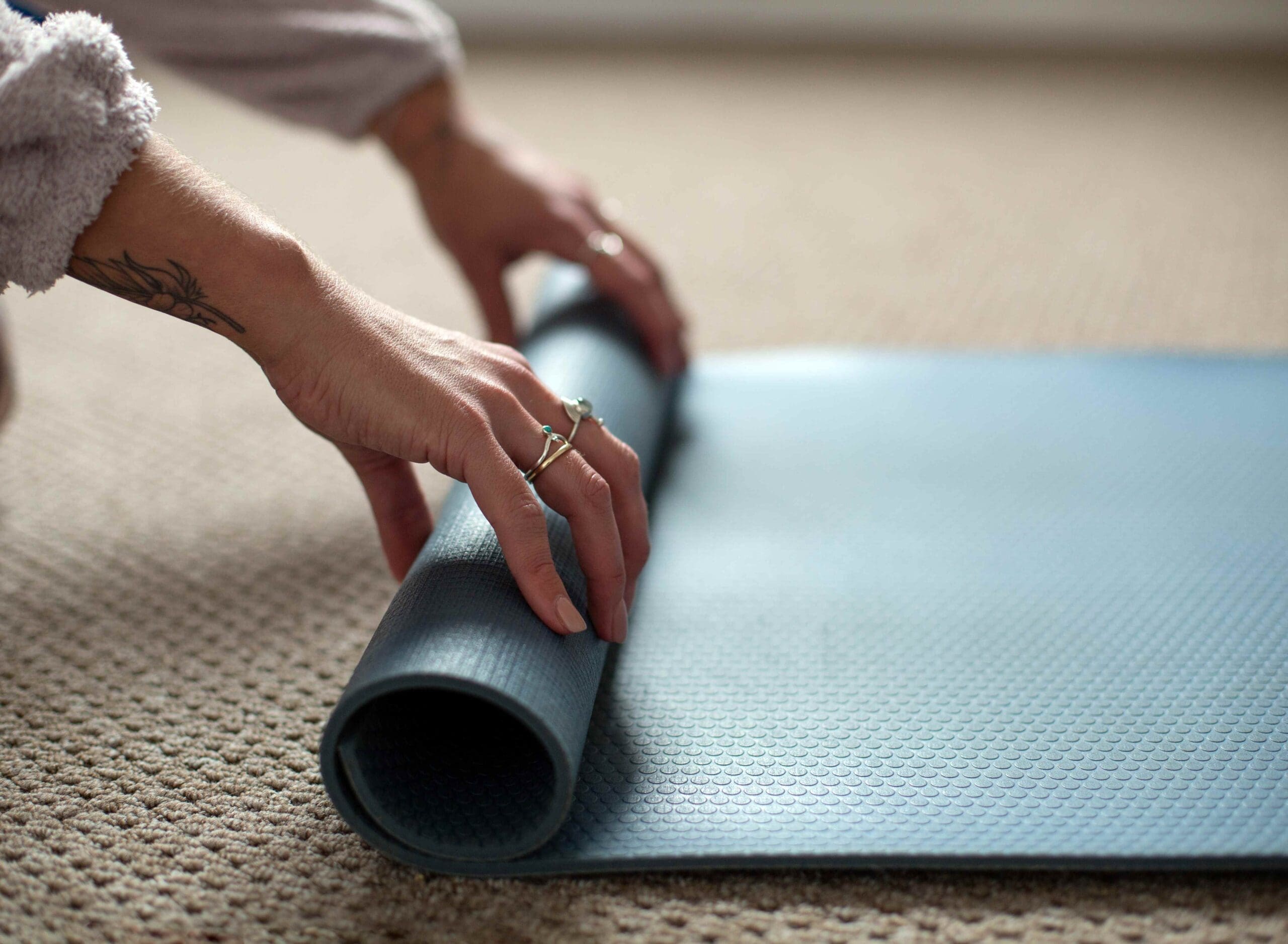 A close up image of some hands rolling up a teal yoga mat.
